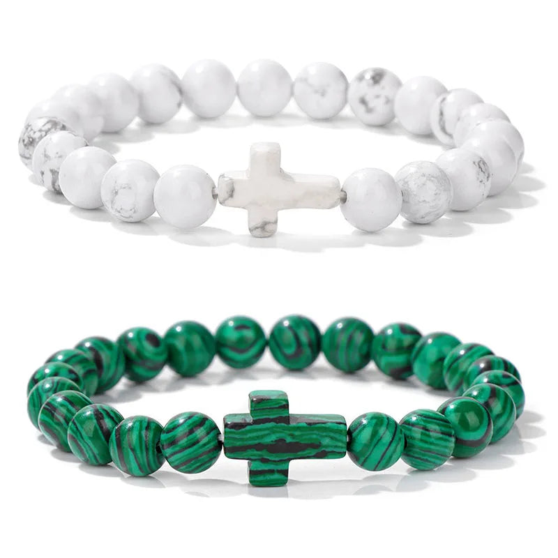 Two beaded bracelets, one white with a cross charm and the other green with a cross charm, on a white background.