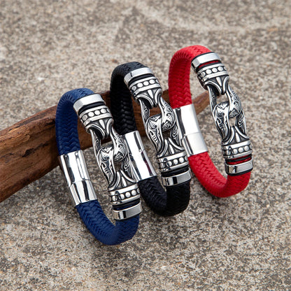 Three braided leather bracelets with ornate silver-toned metal clasp rings, shown in navy blue, black, and red, arranged on a wooden prop against a textured stone background.