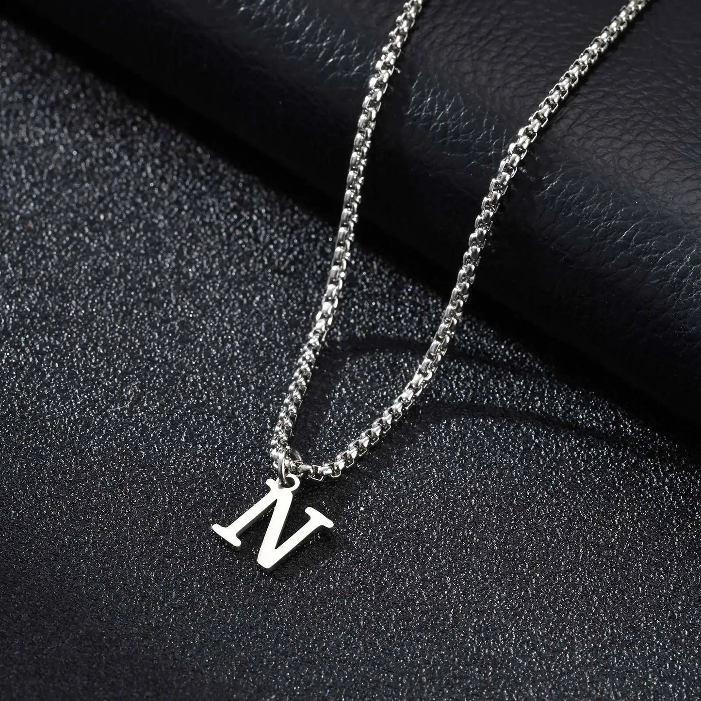 Silver necklace with a 'N' pendant on a black textured surface