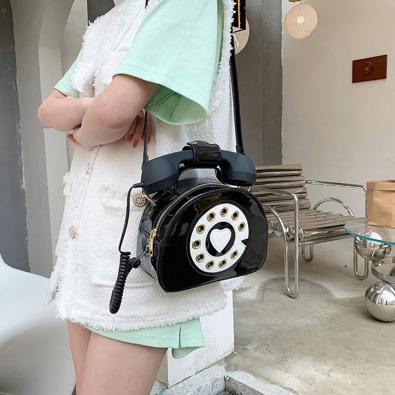 Person holding a black rotary phone-shaped handbag in an indoor setting