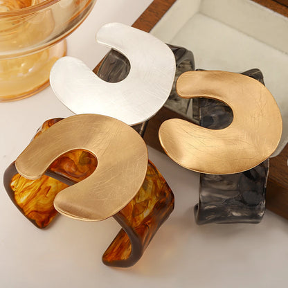 cuff bangles shaped like horseshoe with metallic and amber finishes on a white surface.