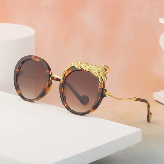 Sunglasses with gold accents and tortoiseshell frame on a white surface with a pinkish-beige background