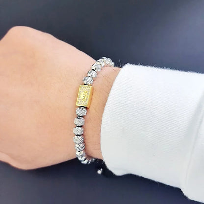Silver bracelet with a gold charm on a wrist against a dark background