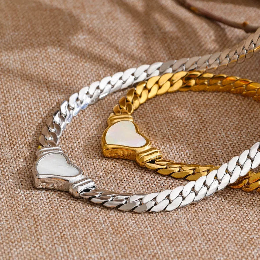 Two necklaces in gold and silver, and a heart-shaped charm on a textured brown surface.