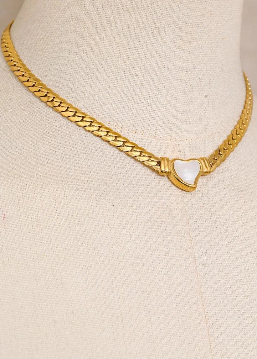 Gold necklace with a heart-shaped pendant on a beige background