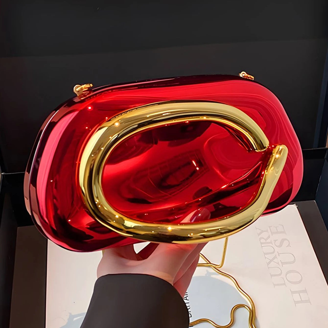 Red and gold handbag held by a person on a dark surface with a magazine underneath