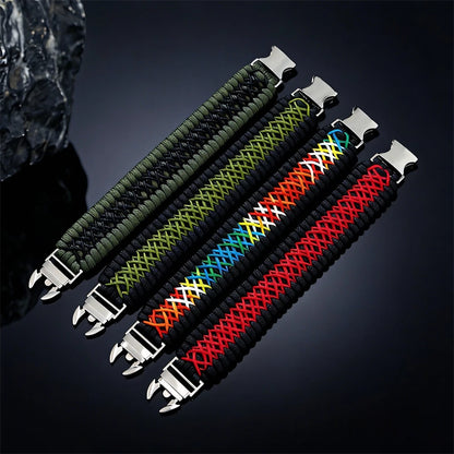 Four braided woven Paracord bracelets with silver metal buckles, arranged diagonally on a dark reflective background. The bracelets feature different colour patterns: olive green and black, light green and black, multicolour rainbow accents, and black with a red braided center.