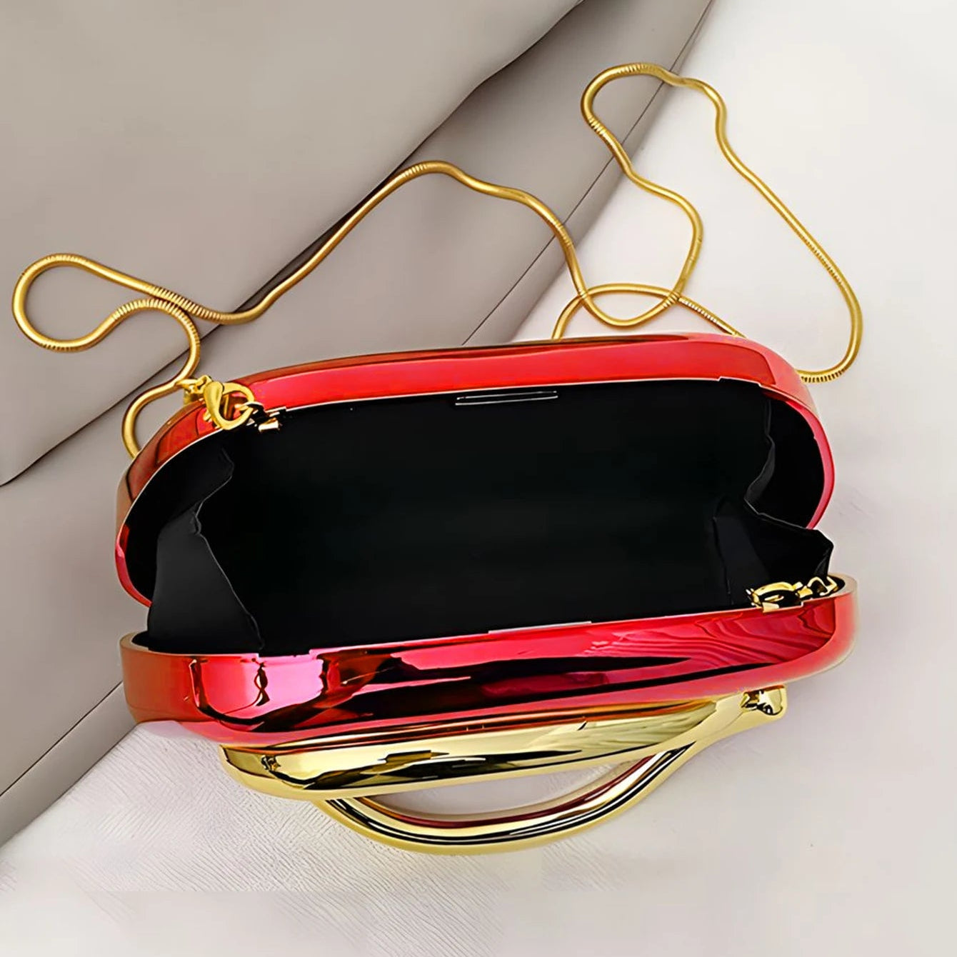 Shiny red handbag with gold handle and clasp on a light background