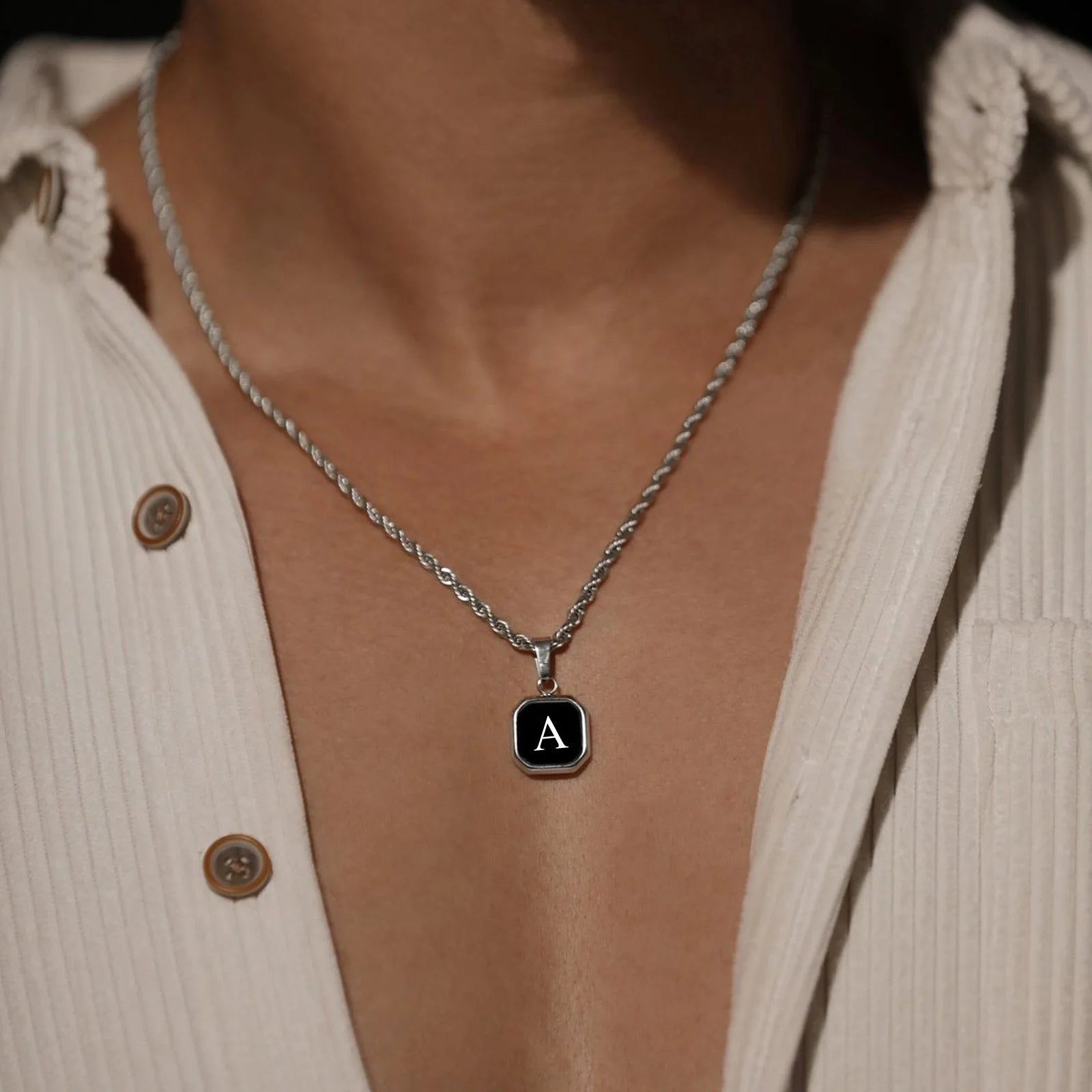 Necklace with a pendant featuring the letter 'A' worn by a person in a beige cardigan.