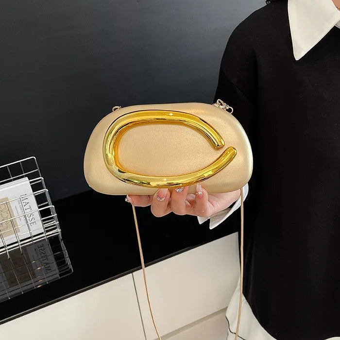 Beige handbag with gold accents held by a person against a black background