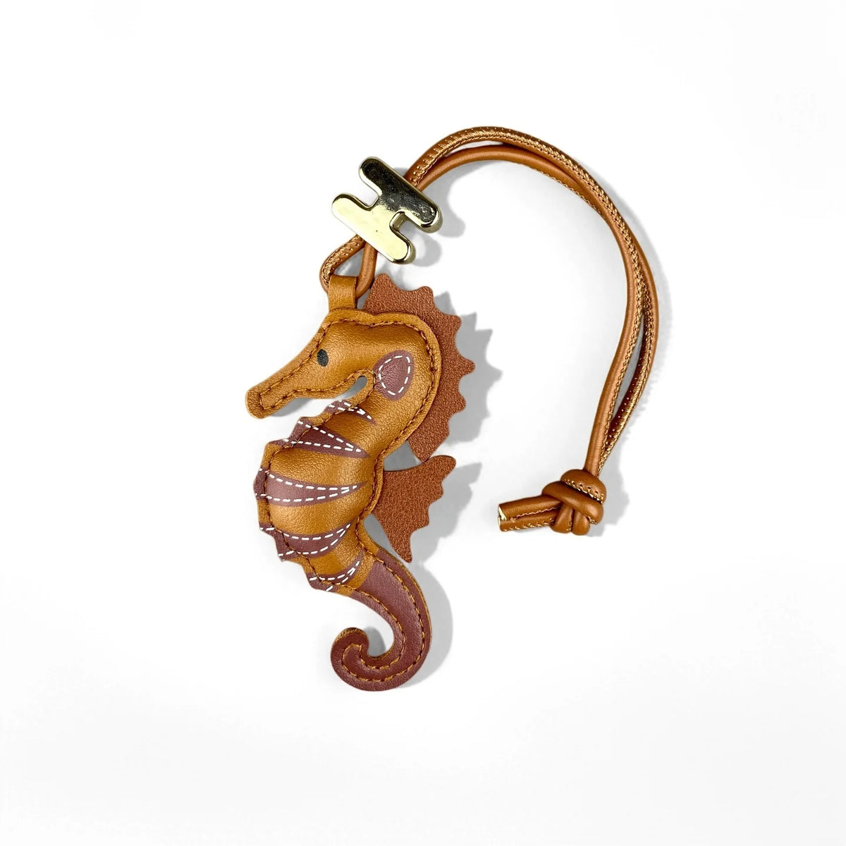 A brown leather seahorse-shaped keychain or bag charm with a tan strap and gold-tone metal hardware, photographed on a clean white background.