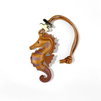 A brown leather seahorse-shaped keychain or bag charm with a tan strap and gold-tone metal hardware, photographed on a clean white background.