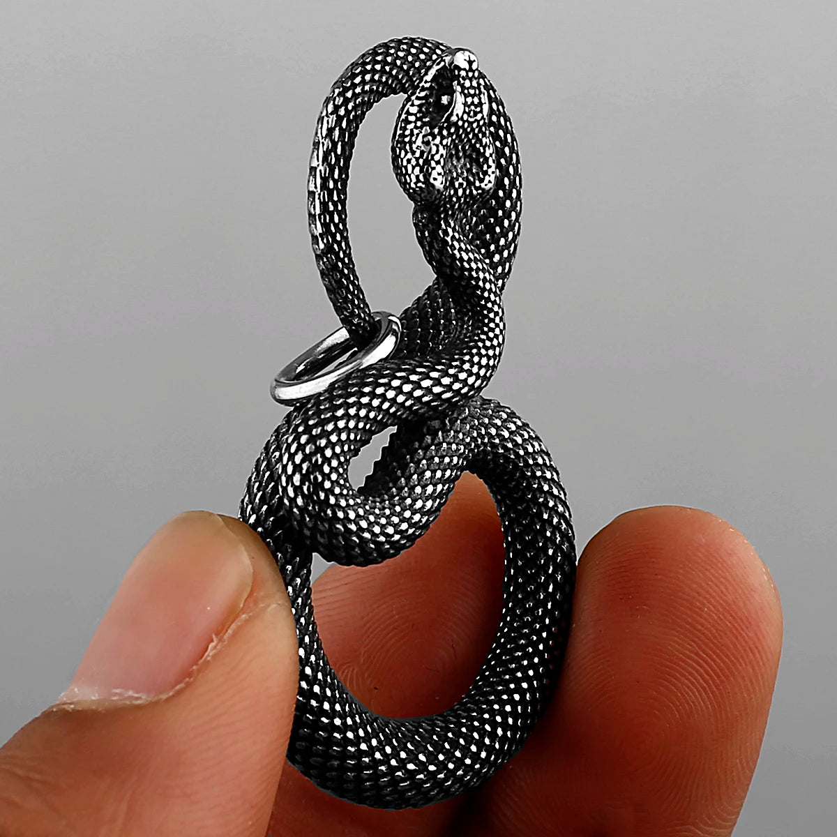Metallic snake-shaped pendant held between fingers against a grey background