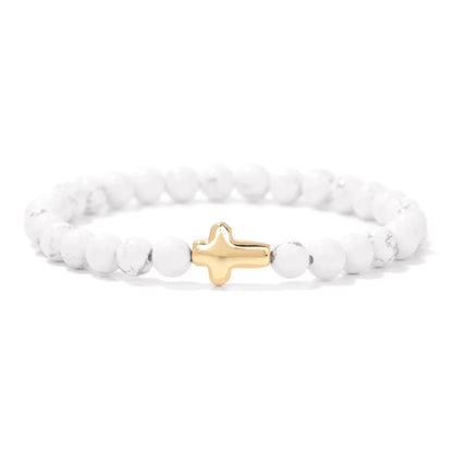 White beaded bracelet with a gold cross charm on a white background