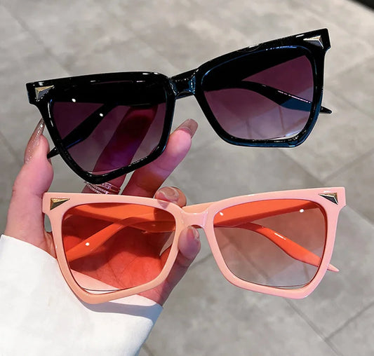 Two pairs of sunglasses, one black and one pink, held by a hand on a light background.