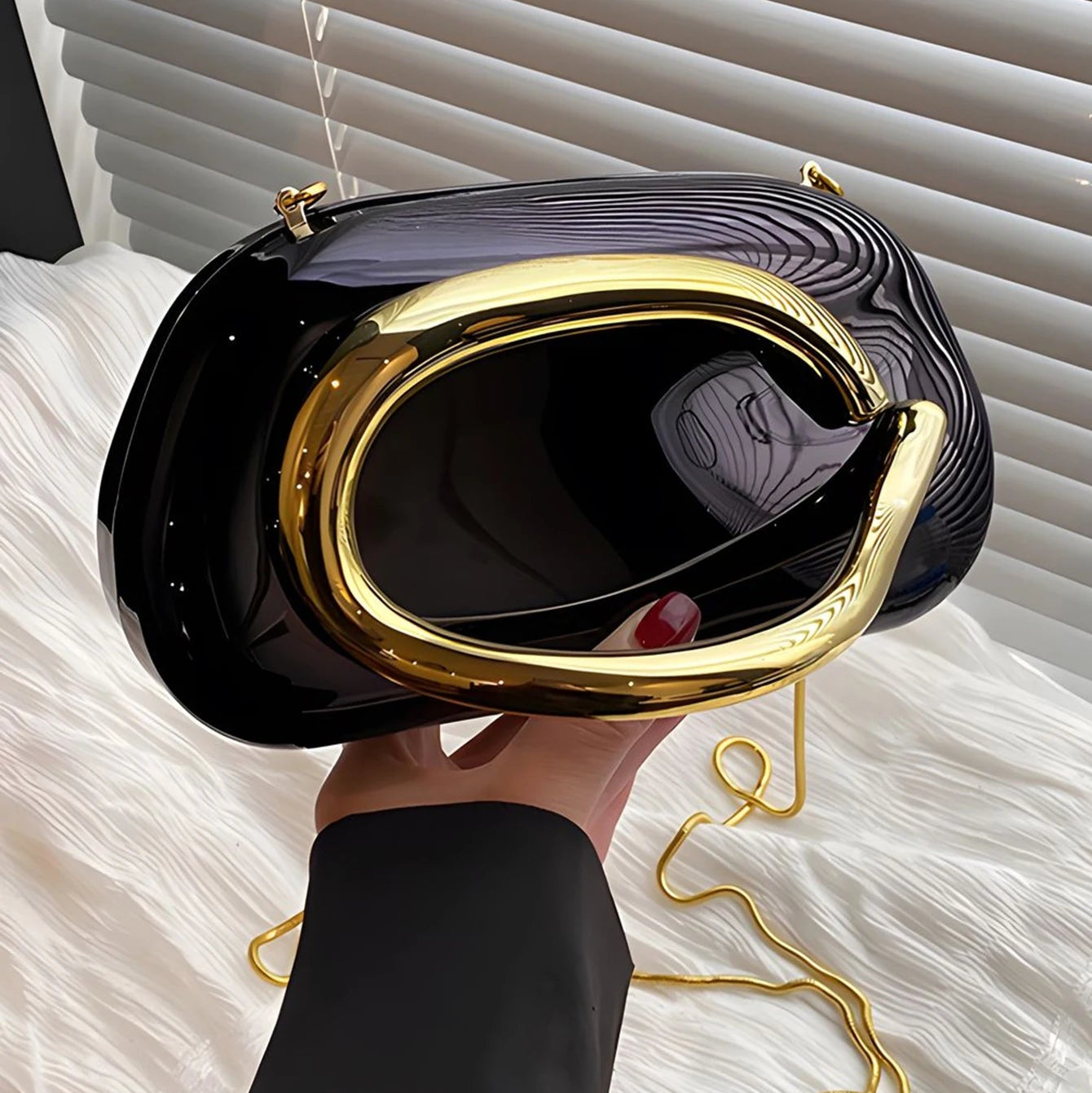 Black clutch with gold accents held by a hand against a white background