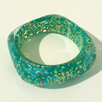 Turquoise acrylic bangle with gold flecks on a white background