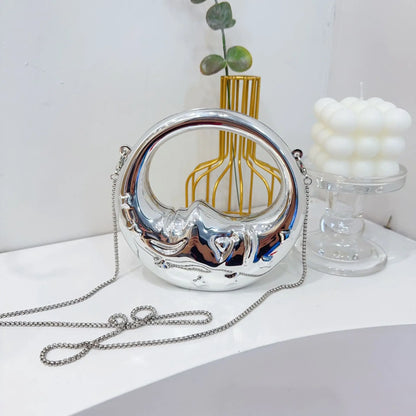 Silver crescent handbag with chain strap on a white surface with decorative items.