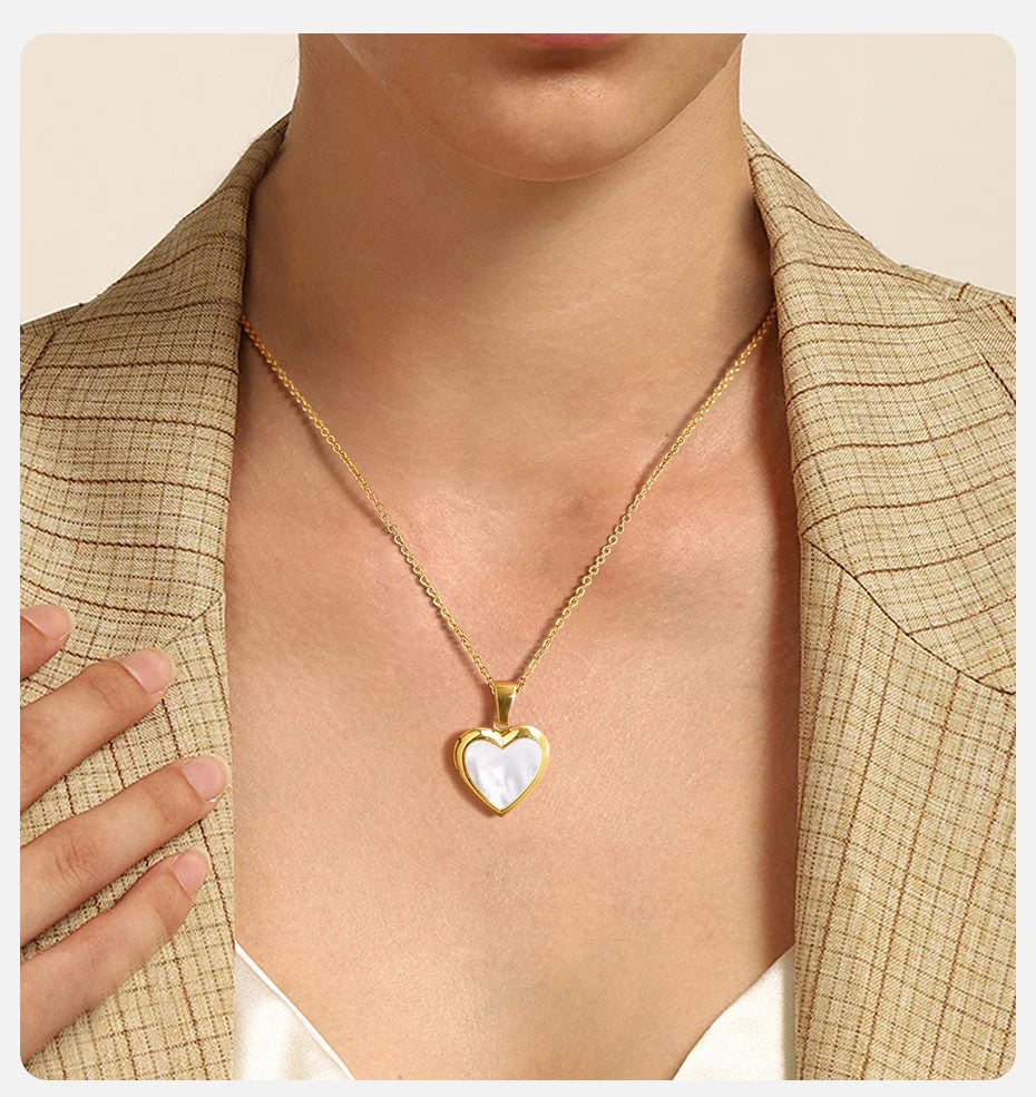 Gold necklace with a heart-shaped pendant worn by a person in a beige jacket.