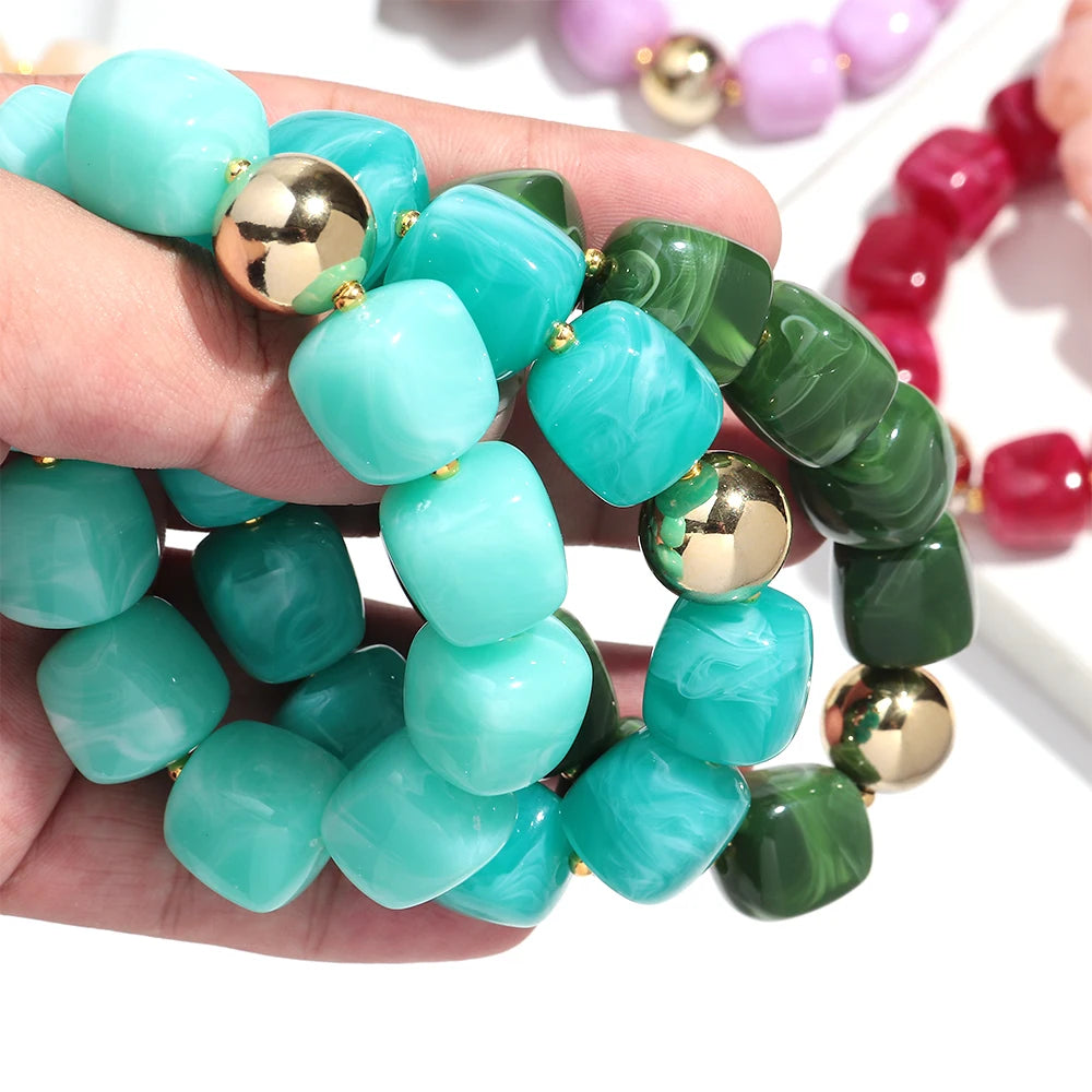 Turquoise and green beaded bracelet with gold accents held in a hand, with more bracelets in the background.