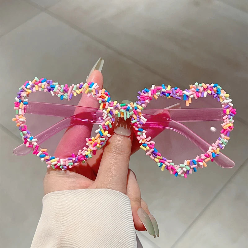 Colourful bow-shaped sunglasses with a transparent frame held by a hand.
