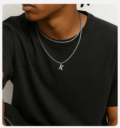 Person wearing a black shirt with a silver necklace featuring a letter 'K' pendant.