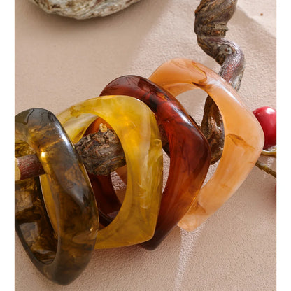 Set of four multicoloured resin bracelets on a textured surface with natural elements.