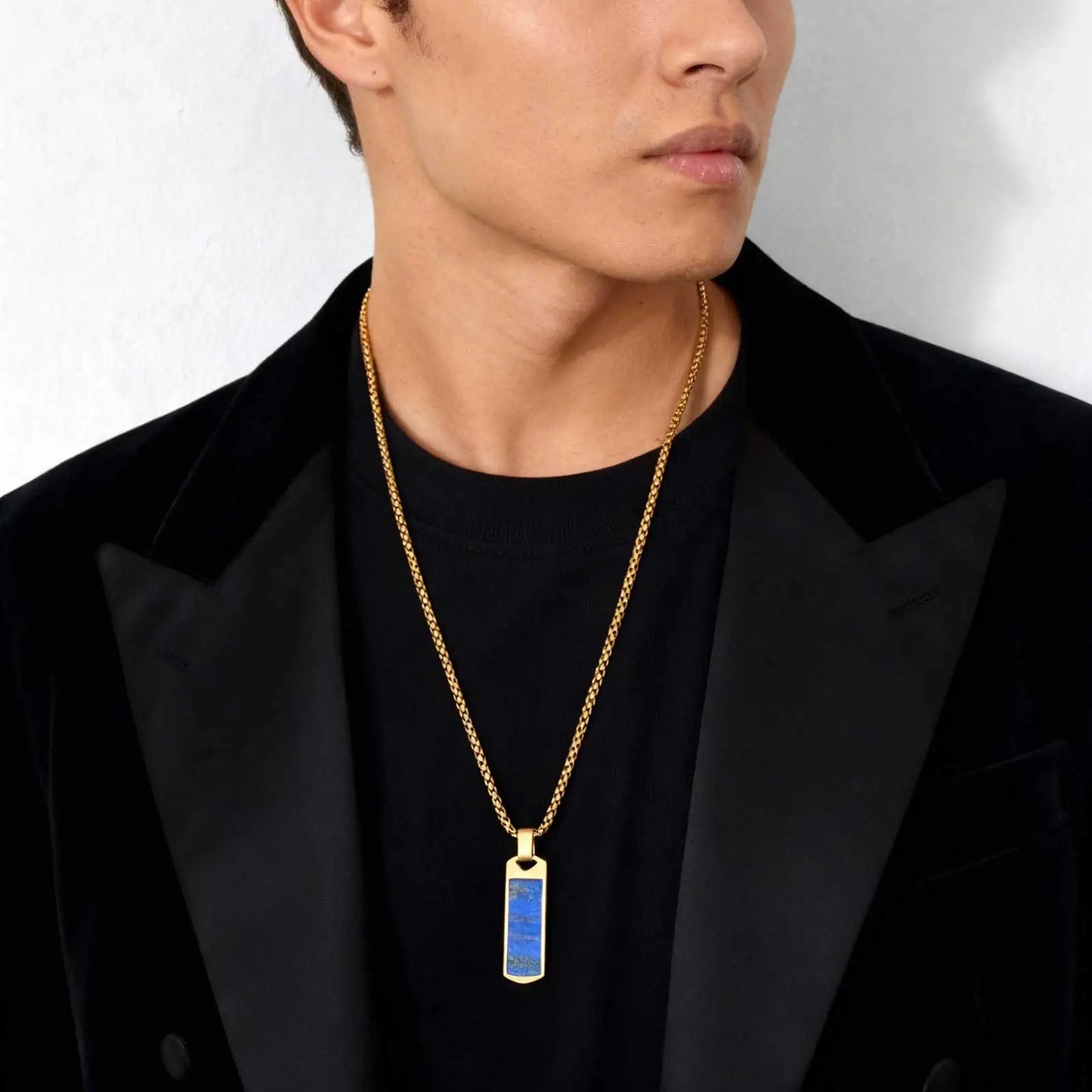 Man wearing a black jacket with a gold necklace featuring a blue pendant.