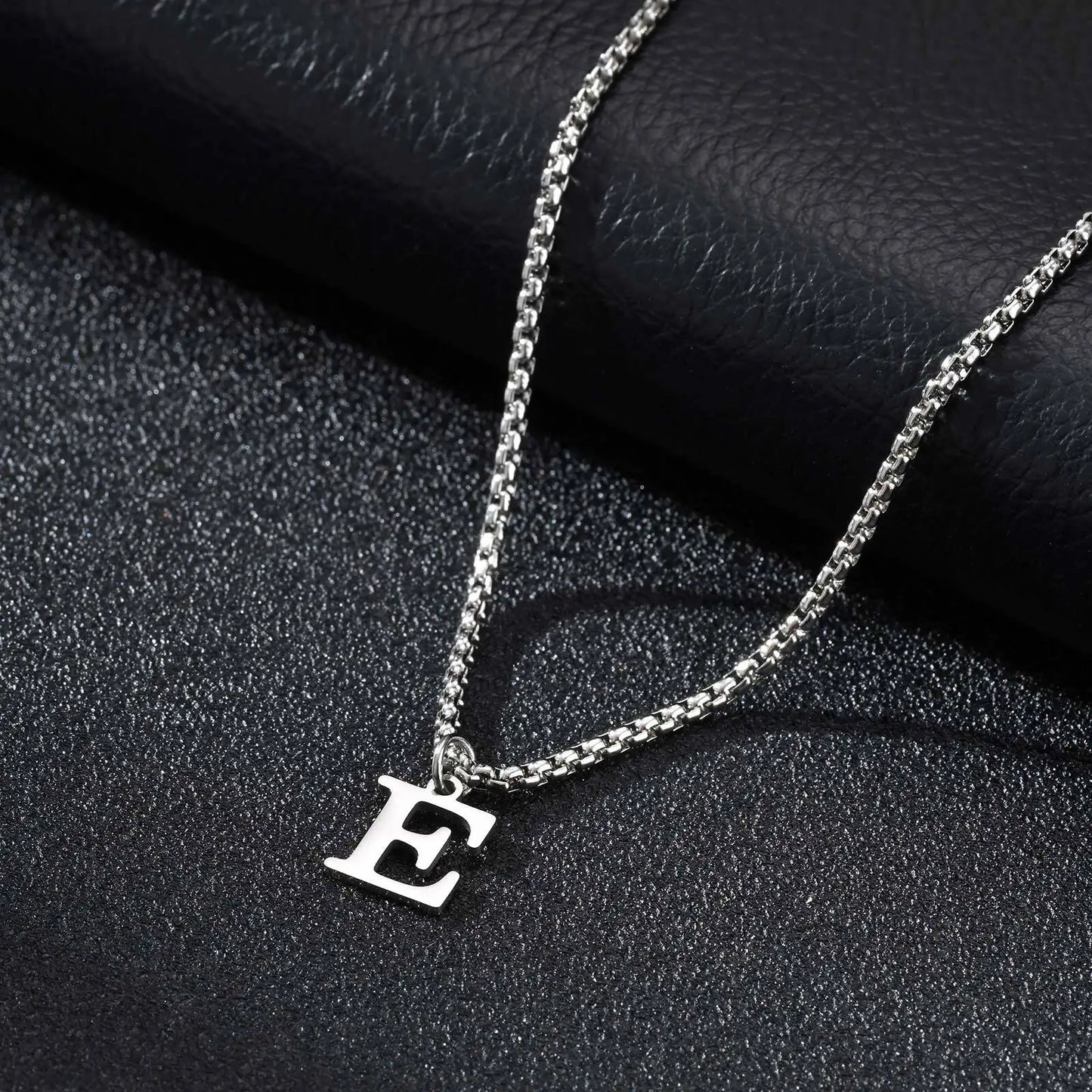 Silver necklace with a 'E' pendant on a dark textured surface