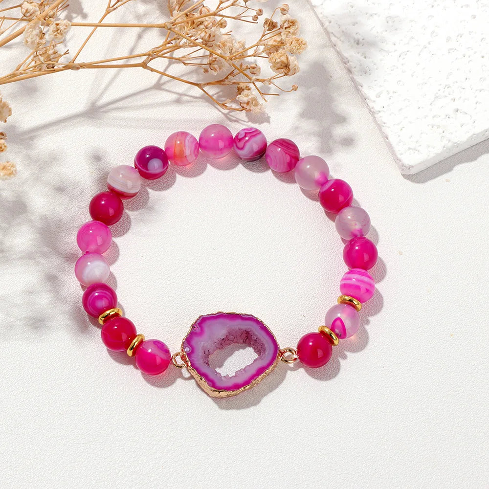 Pink beaded bracelet with a geode charm on a white surface with dried flowers.