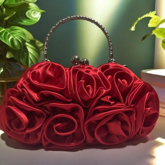 Red rose-shaped handbag on a white surface with green plants in the background