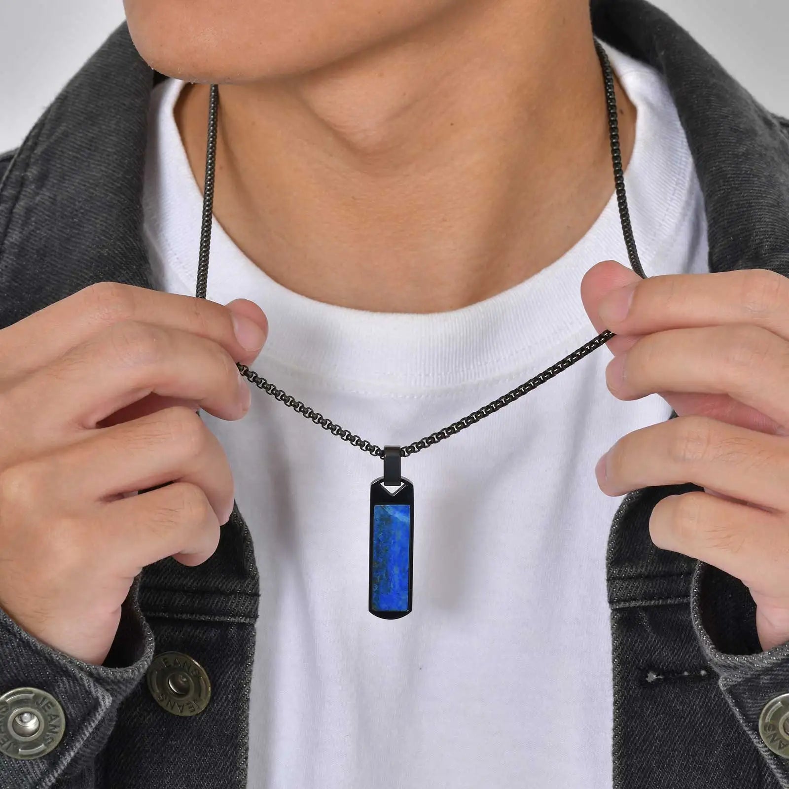 Person holding a necklace with a blue pendant against a white background