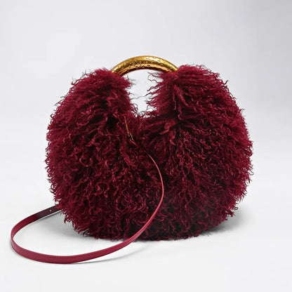 Maroon fuzzy handbag with gold handle on a light grey background