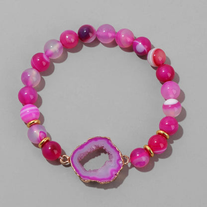 Pink beaded bracelet with a geode charm on a grey background