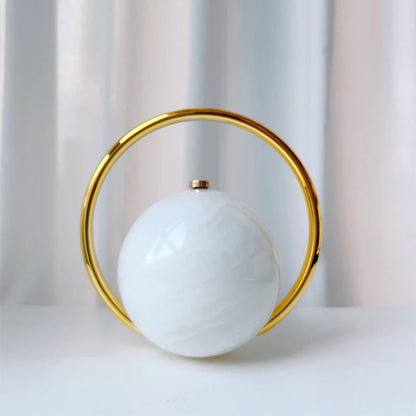 Decorative clutch bag with a white sphere and gold circular frame on a light background
