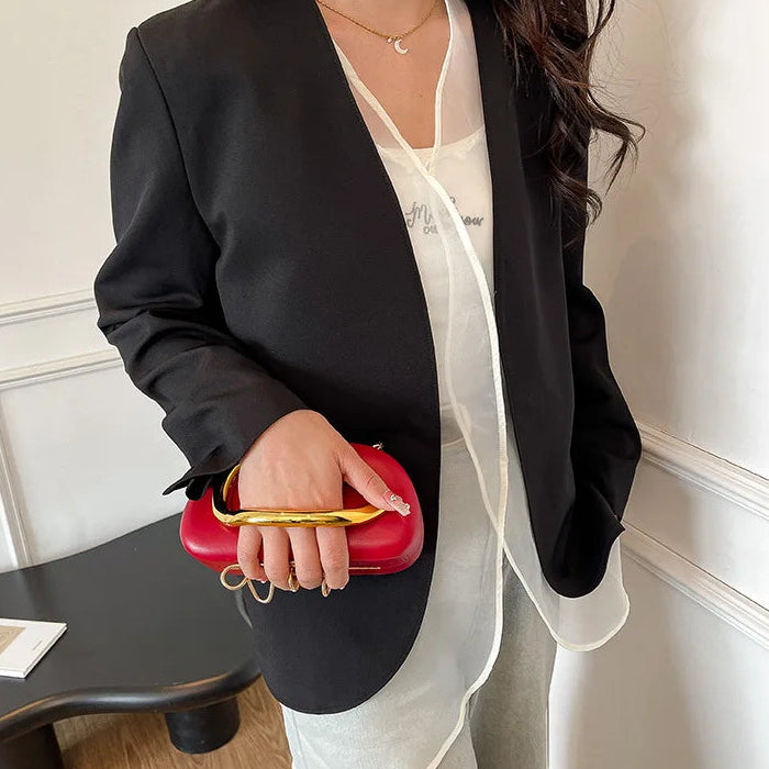 Person wearing a black blazer and white shirt, holding a red clutch.