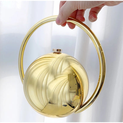 Gold circular handbag held by a hand against a white background