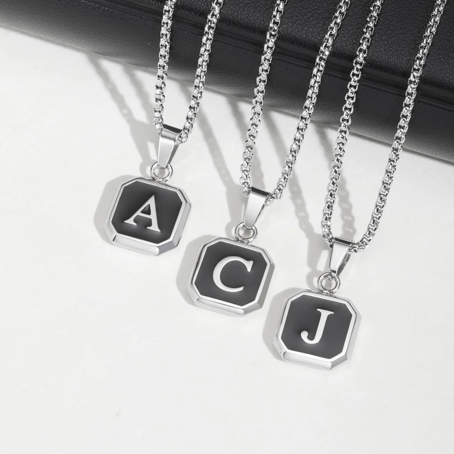 Three silver necklaces with letter pendants on a white background