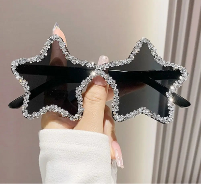 Star-shaped sunglasses with black frame and rhinestone details held by a hand.