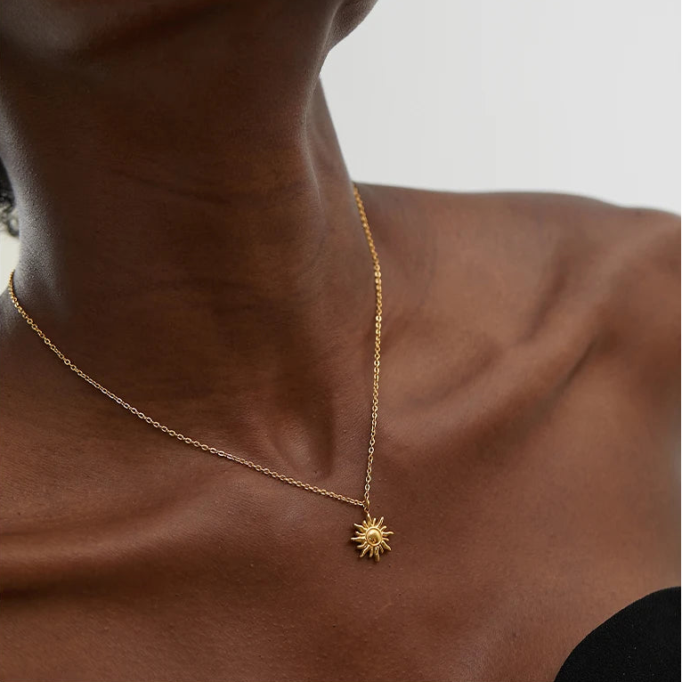Person wearing a gold necklace with a sun pendant on a neutral background