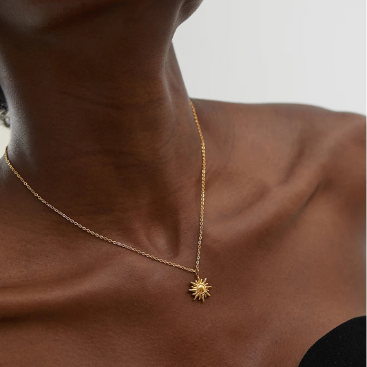 Person wearing a gold necklace with a sun pendant on a neutral background