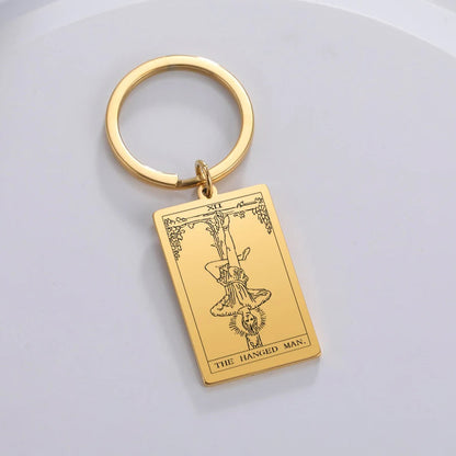 Gold keychain with 'The Hanged Man' tarot card design on a light grey background
