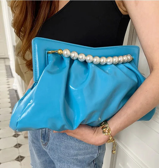 Blue clutch with pearl embellishments held by a person in a casual setting.