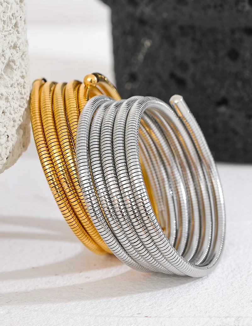 Set of gold and silver bracelets on a textured surface with a neutral background.