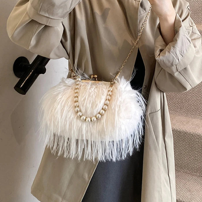 Person holding a beige handbag with feather details and a pearl chain.