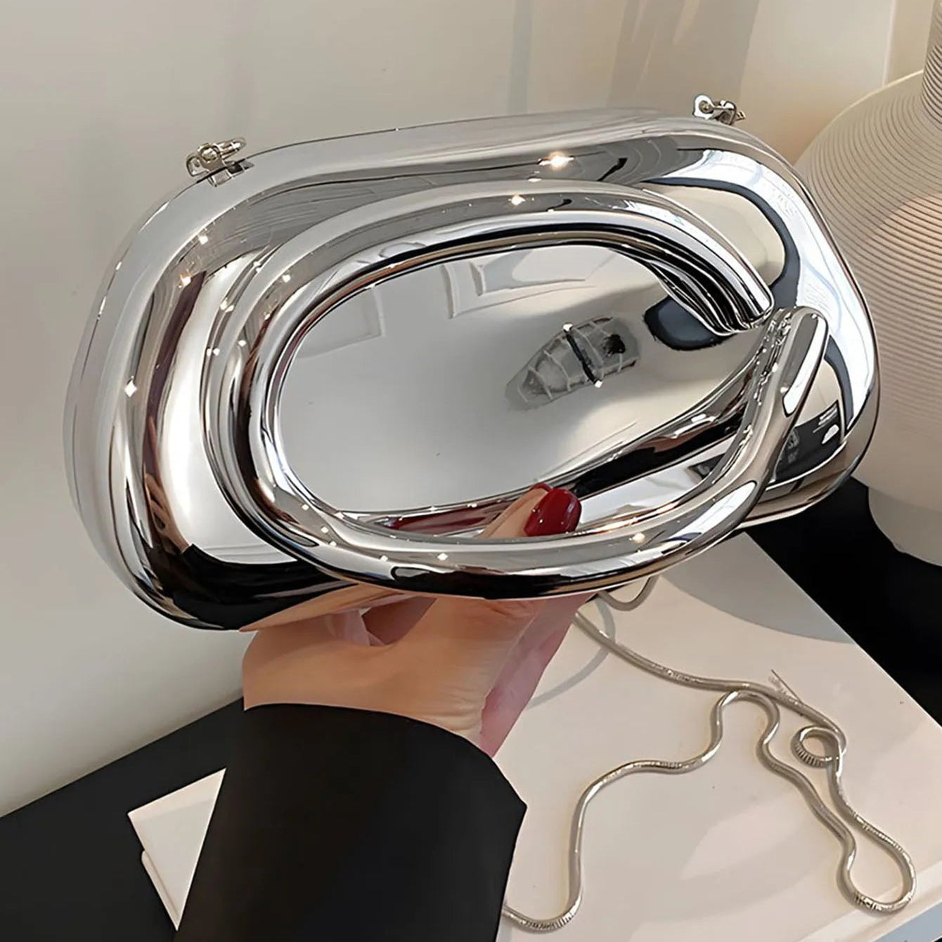 Silver handbag held by a person against a neutral background