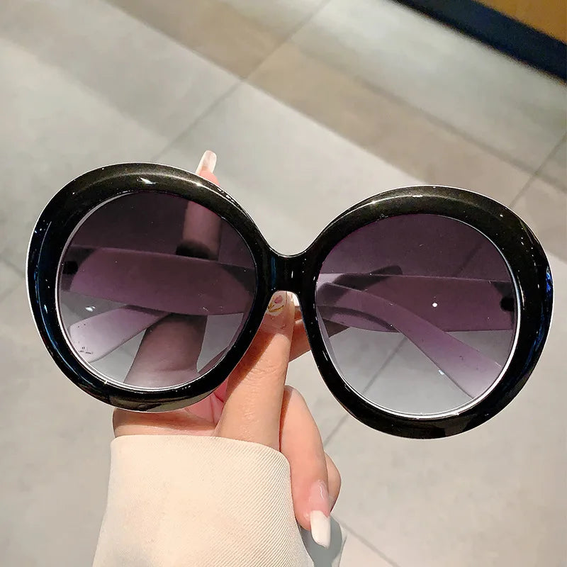 Black frame with white accents sunglasses held by a hand on a light grey background