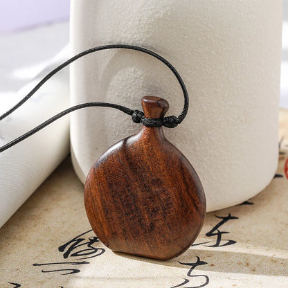 Wooden pendant on a black cord with a white vase and calligraphy in the background