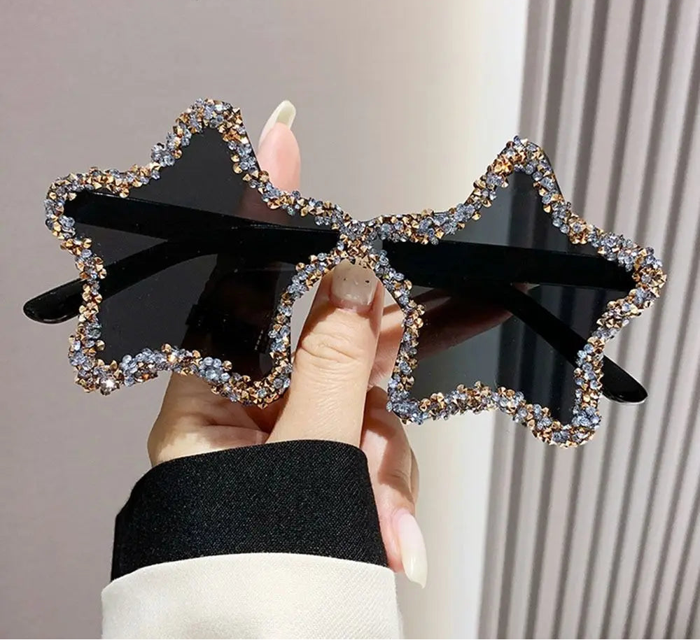 Star-shaped sunglasses with black frame and rhinestone details held by a hand.