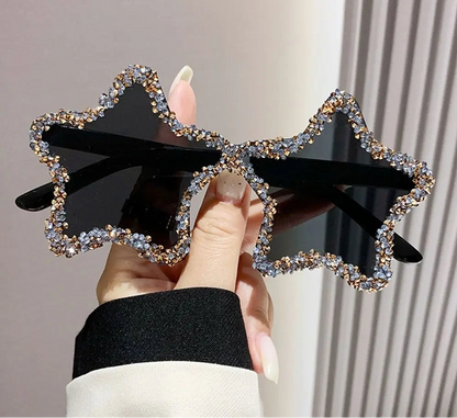Star-shaped sunglasses with black frame and rhinestone details held by a hand.